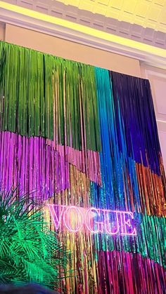 a colorful wall hanging from the ceiling in front of a window with palm trees and neon lights