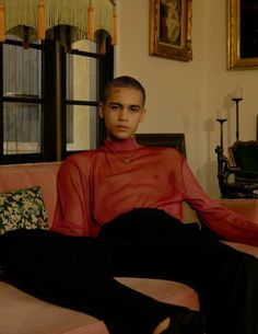 a young man sitting on top of a couch in a living room next to a window