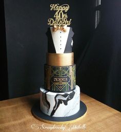 a three tiered cake decorated with black and white designs, gold lettering and a bow