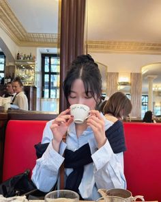 a woman sitting at a table drinking from a cup