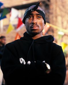 a man in a black hoodie is standing with his arms crossed and looking at the camera