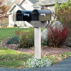 two mailboxes in front of a house on the side of a road with grass and flowers