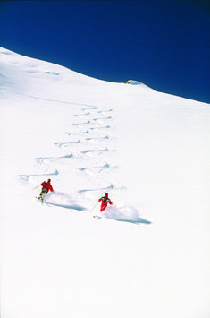 two people skiing down a snow covered slope with tracks in the snow on skis