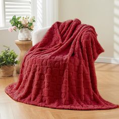 a red blanket sitting on top of a wooden floor next to a white chair and potted plant