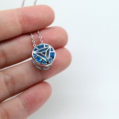 a hand holding a blue and white necklace with an arrow on the bottom, in front of a white background