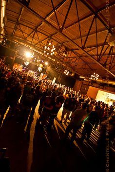 a large group of people are standing in a room with lights on the ceiling and one person is holding a cell phone