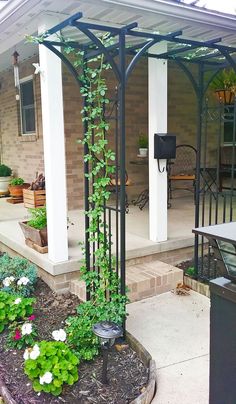 an outdoor covered patio area with flowers and plants growing on the side of the house