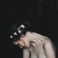 a woman with flowers in her hair is looking down at the ground as she holds her hand over her face