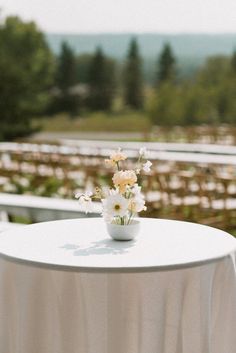 a white table topped with a vase filled with flowers next to rows of chairs in the background