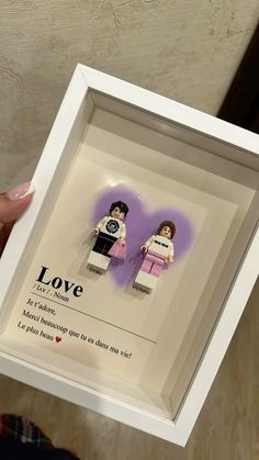 someone is holding up a lego minifigure in a white frame that says love