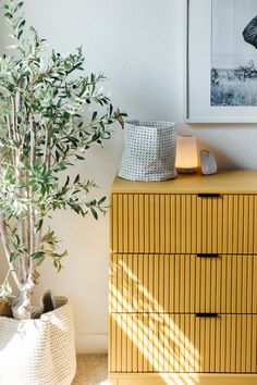 a yellow dresser with two baskets and a potted plant