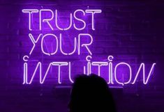 a woman standing in front of a neon sign that says trust your institution on it