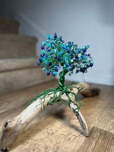 a blue beaded tree sits on top of some driftwood in front of stairs