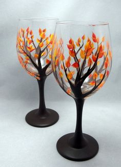 two wine glasses with painted leaves on them are sitting side by side in front of a white background