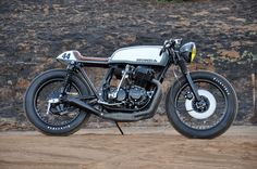 a white and black motorcycle parked on top of a dirt road next to a stone wall