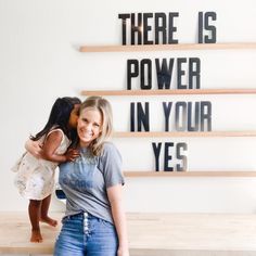 two women standing next to each other in front of a wall with words on it