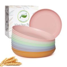 a stack of pink plates next to a box of wheat seed stalks on a white background