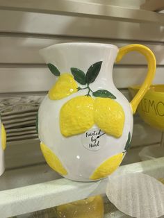 a yellow and white vase with lemons painted on it's sides sitting on a shelf