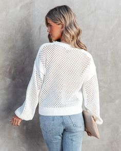 a woman in jeans and a white sweater is standing against a gray wall with her back to the camera