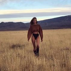 a woman in a bodysuit walking across a dry grass field