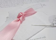 a pair of scissors sitting on top of a piece of paper next to a pink ribbon