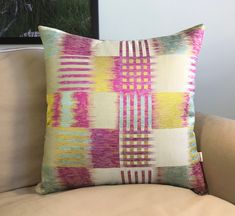 a colorful pillow sitting on top of a couch next to a framed painting in a living room