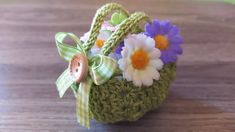 a crocheted basket with flowers and a wooden button on it sitting on a table