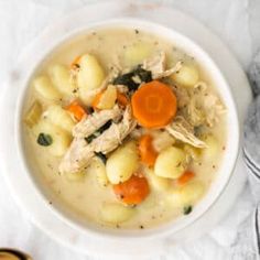 a bowl of chicken and dumpling soup on a white tablecloth next to a wooden spoon