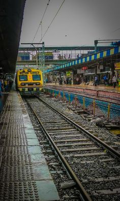 two trains on tracks next to each other at a train station with people standing near by