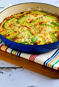 a casserole dish with green peppers and cheese in a blue pan on a wooden board