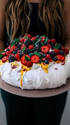 a woman holding a cake with berries and cream frosting on the top, in front of her