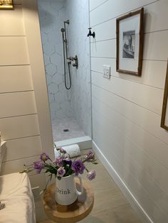 a vase with flowers in it sitting on a table next to a bathtub and shower