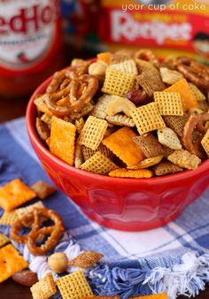 a red bowl filled with cheetos and pretzel snack mix on top of a table