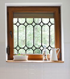 a window in a white tiled bathroom with potted plants on the ledge and watering can