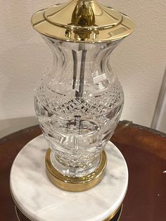 a clear glass vase sitting on top of a white marble table next to a gold lid