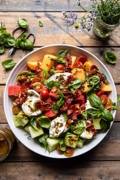 a salad with tomatoes, cucumbers and other vegetables on a wooden table next to a glass of beer