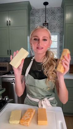 a woman holding two pieces of cheese in her hands while standing next to a counter