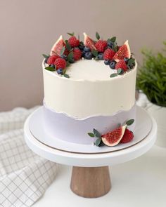 a white cake topped with fresh fruit on top of a wooden stand next to a potted plant