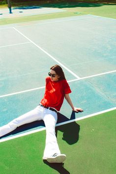 a woman sitting on the edge of a tennis court with her legs spread out and feet crossed