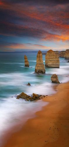 the beach is lined with large rocks under a colorful sky at sunset or sunrise time