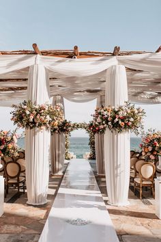 an outdoor wedding setup with white draping and floral arrangements on the aisle, overlooking the ocean