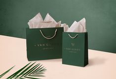 two green shopping bags sitting on top of a table next to a palm leaf and plant