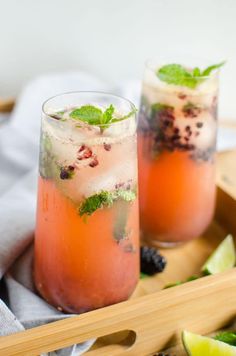 two glasses filled with drinks sitting on top of a wooden tray