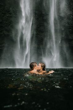 two people are kissing in front of a waterfall while standing in the water with their arms around each other