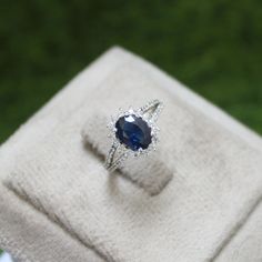 an engagement ring with a blue sapphire sits on top of a white cloth in front of green grass