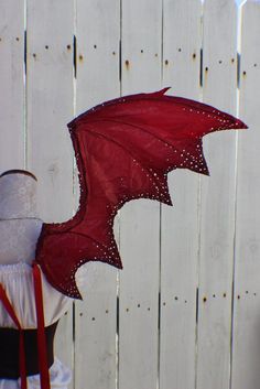 a red dragon kite is being held by a woman's head in front of a white fence