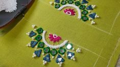 two pieces of embroidered fabric on top of a green cloth with white beads and pink flowers