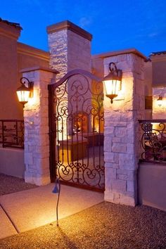 an iron gate is lit up at night in front of a house with lights on