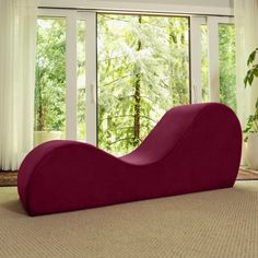 a large red chaise lounger sitting in front of a window next to a potted plant