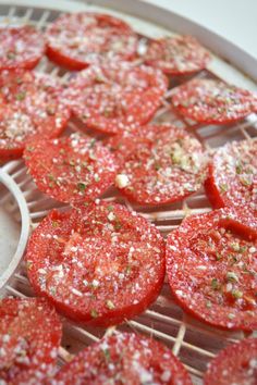 sliced tomatoes sitting on top of a rack with seasoning next to the whole tomato